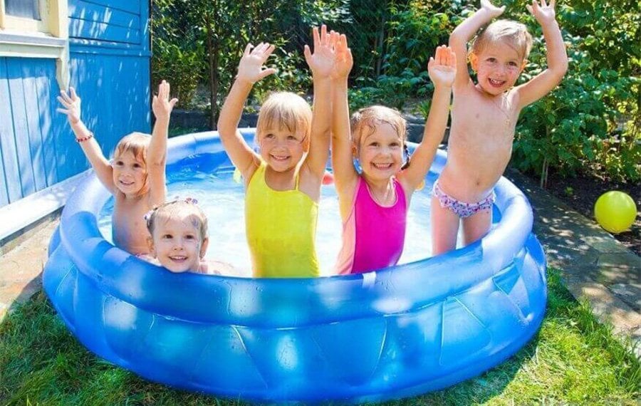 Açık havada şişme çocuk havuzunda yetişkin gözetiminde eğlenen çocuklar